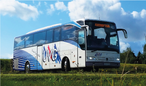 Ein Reisebus, ein sogenannter PlusBus, steht auf einer grünen Fläche in der Natur.