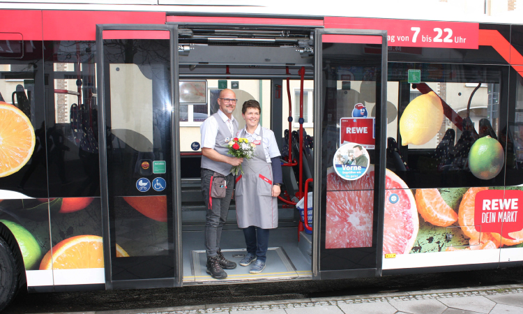 Bus, der mit Werbestickern der Marke Rewe versehen ist.