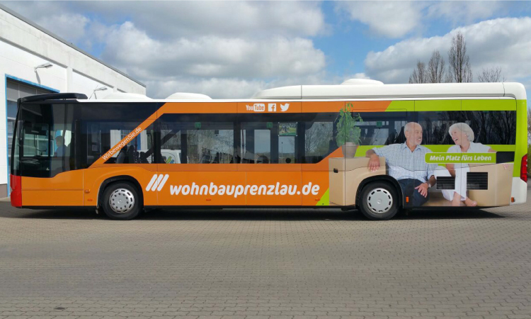 Ein Bus, der mit Werbestickern der Marke Wohnbau Prenzlau versehen ist.